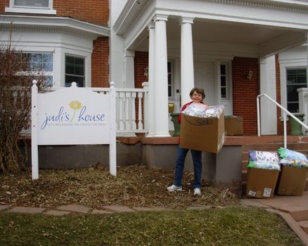 JoAnn Zimmerman holding a box of pillows in front of Judi's House in  Denver