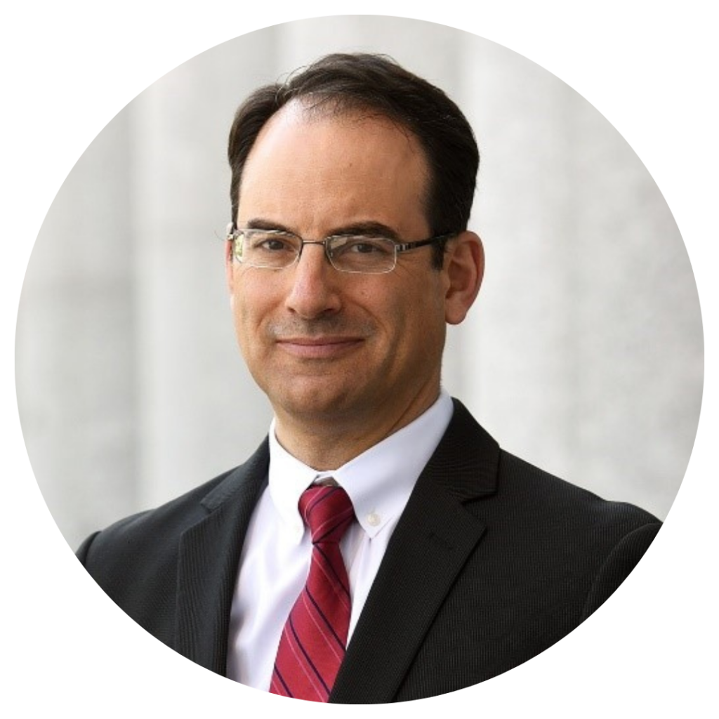 Colorado Attorney General, Phil Weiser, in a black suit with red tie against gray background