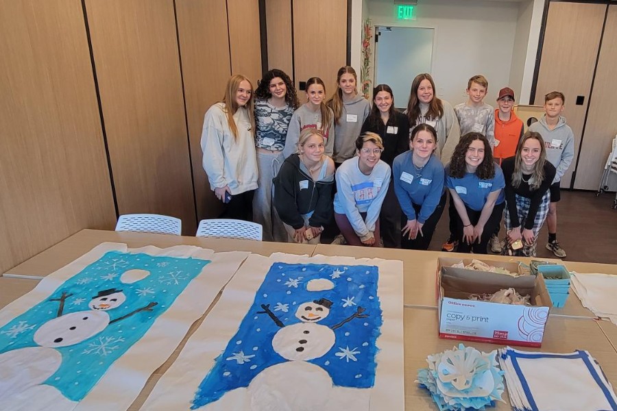 Group of youth volunteers pose for photo in front of holiday decorations and quilt squares they helped make for Judi's House programs.
