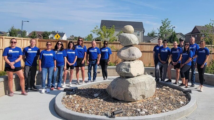 Corporate volunteers from PepsiCo pose in matching blue shirts by Judi's House cairn statue after a successful team volunteer day. Volunteer at Judi's House