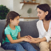 woman sitting on couch explaining something to young girl while holding hands