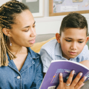 woman with braided hair reading a children's book with a younger male child laying on a couch