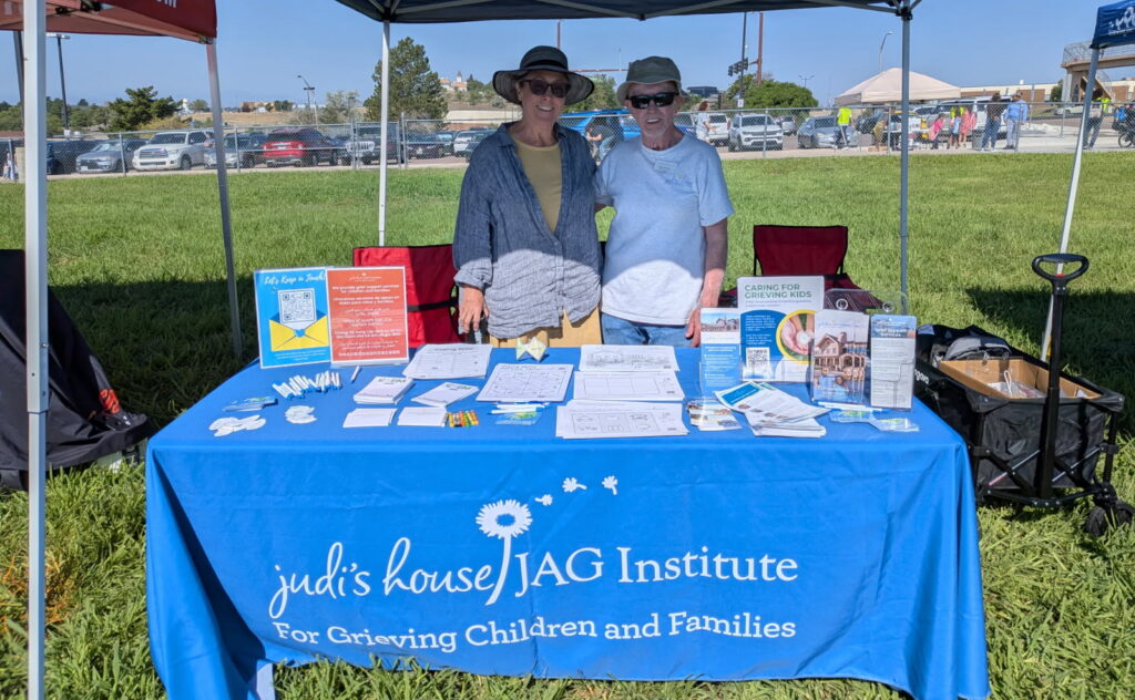 a man and a woman standing behind a table with a blue tablecloth featuring the Judi's House logo
